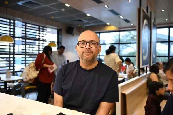 Man sitting in busy cafe, wearing glasses.